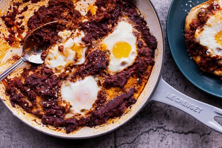 a skillet of eggs in purgatory with a plate to the side of the eggs on garlic bread toast