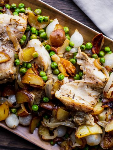 a platter of chicken onions peas and potatoes