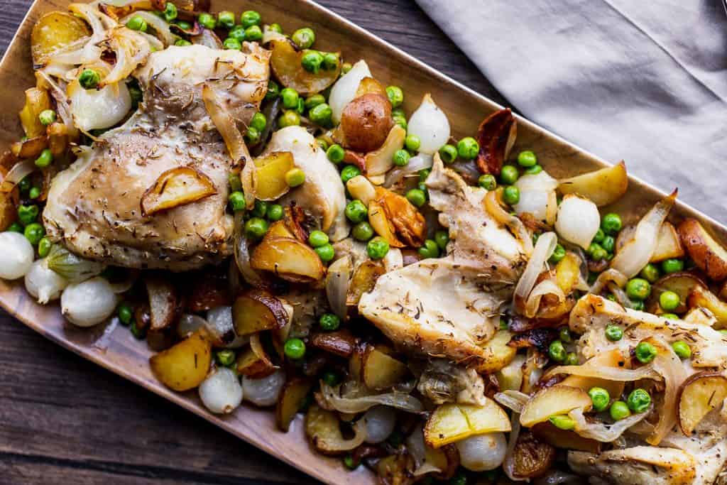 platter of roasted chicken with peas and pearl onions