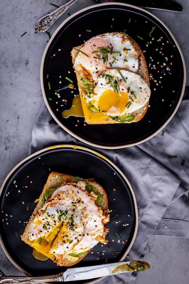 two pieces of avocado toast with two eggs on each toast, broken open to show yolks