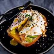 egg topped with chives and everything bagel seasoning on a piece of toast with avocado, the yolk is broken open so the inside is spilling out onto the plate.