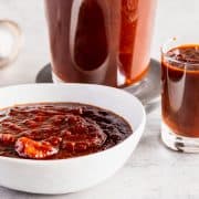 a bowl of BBQ sauce with a small shot glass full and a ladle