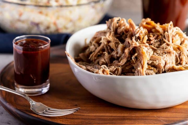 bowl of pulled pork with a side of bbq sauce and coleslaw