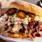 BBQ pork sandwich on a plate with jalapenos poking out from under the bun