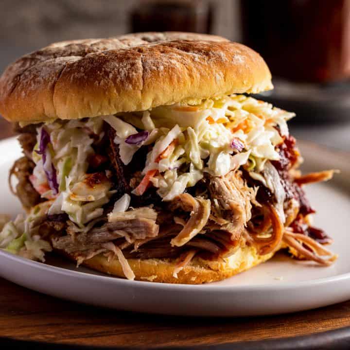 coleslaw piled on a pork sandwich with bbq sauce in the background